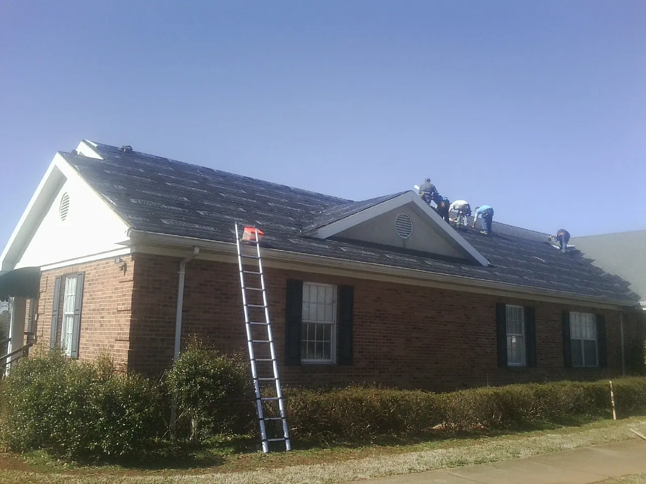 Crew tearing shingles off a brick ranch roof with a ladder set — Metal Roof Repair work by our crew in Elkton